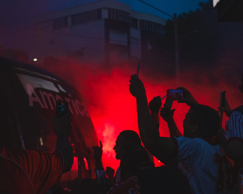 Hinchas del América de Cali con bengalas rojas reciben el bus del equipo en Cali